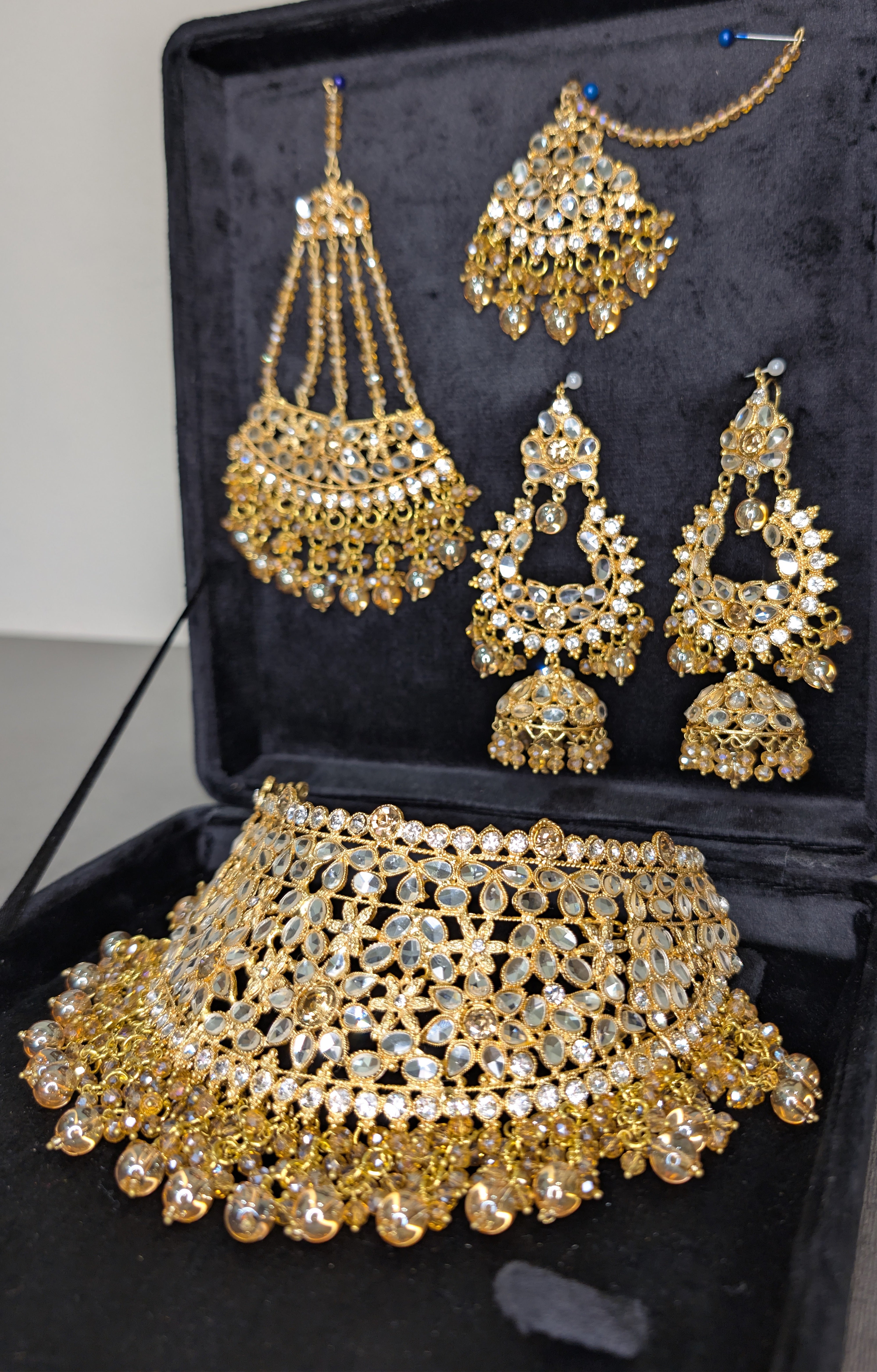 Gold jewelry set including necklace, earrings, and choker on a black velvet box.